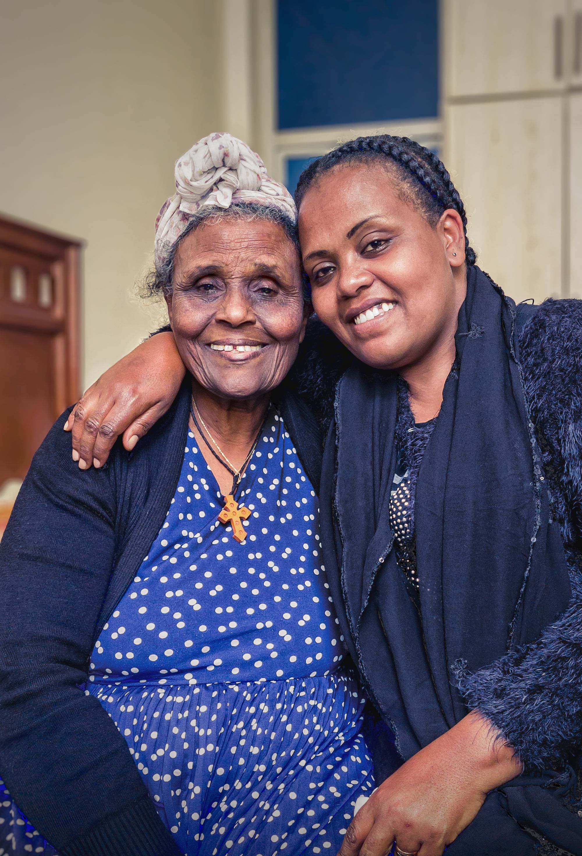 Une femme âgée et une femme plus jeune, joue contre joue, sourient.